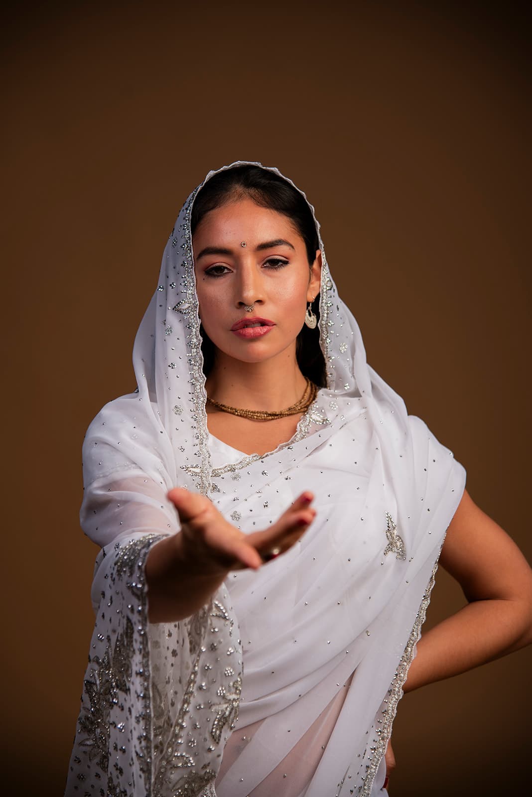 Vinodini offering an open hand, wearing a white and silver sari.