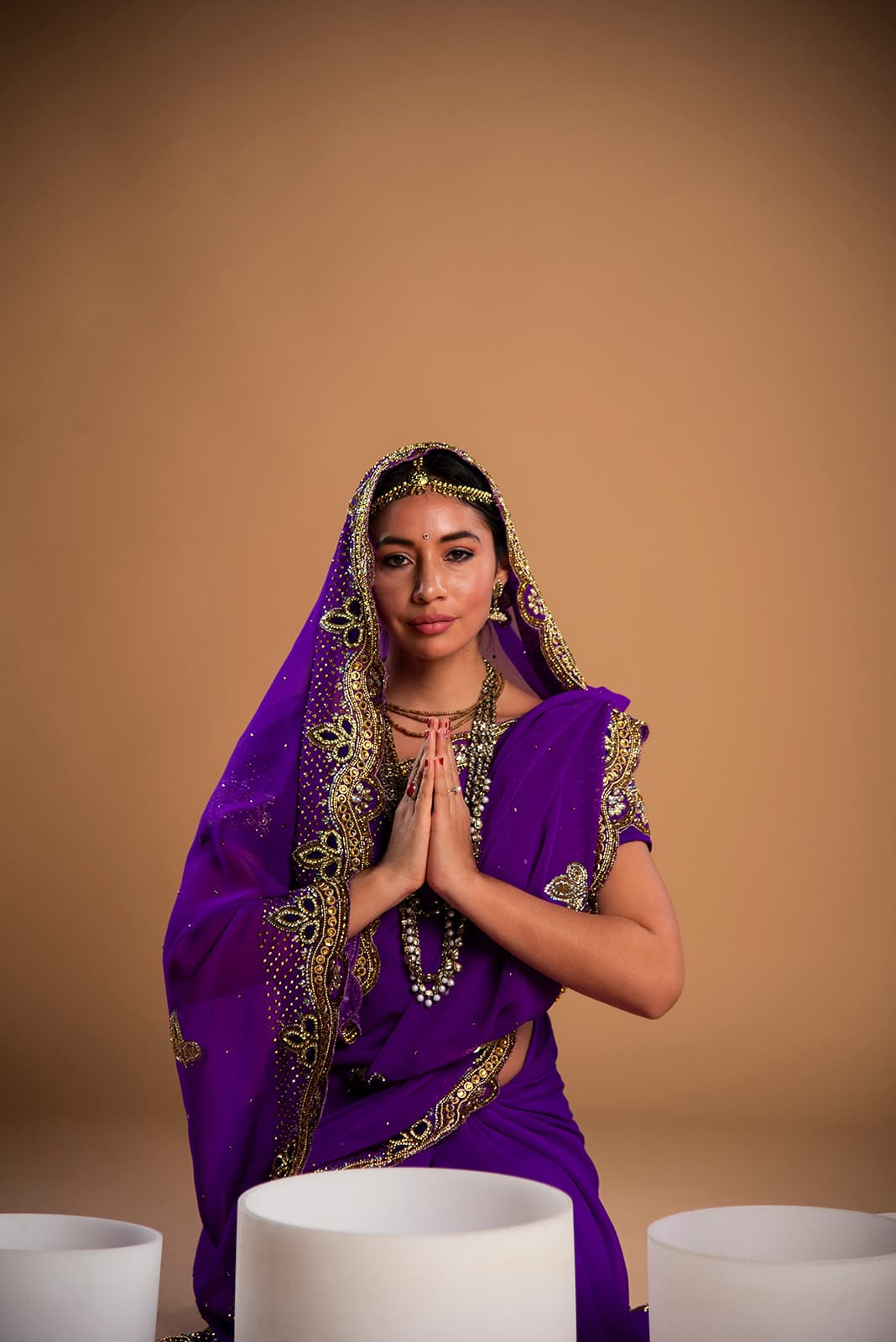 Vinodini Dasi in a purple and gold sari, with her hands together in prayer.